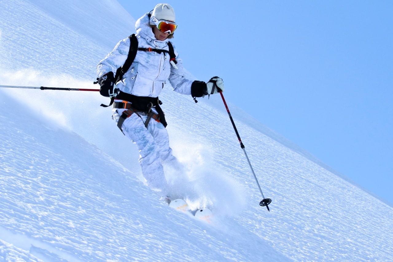 Skier dressed in a white snowsuit and bright goggles navigates a freshly powdered mountain in Alaska.